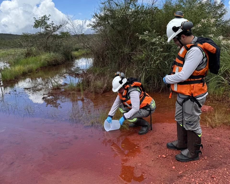 Duas pessoas com equipamentos de proteção realizando coleta de água.