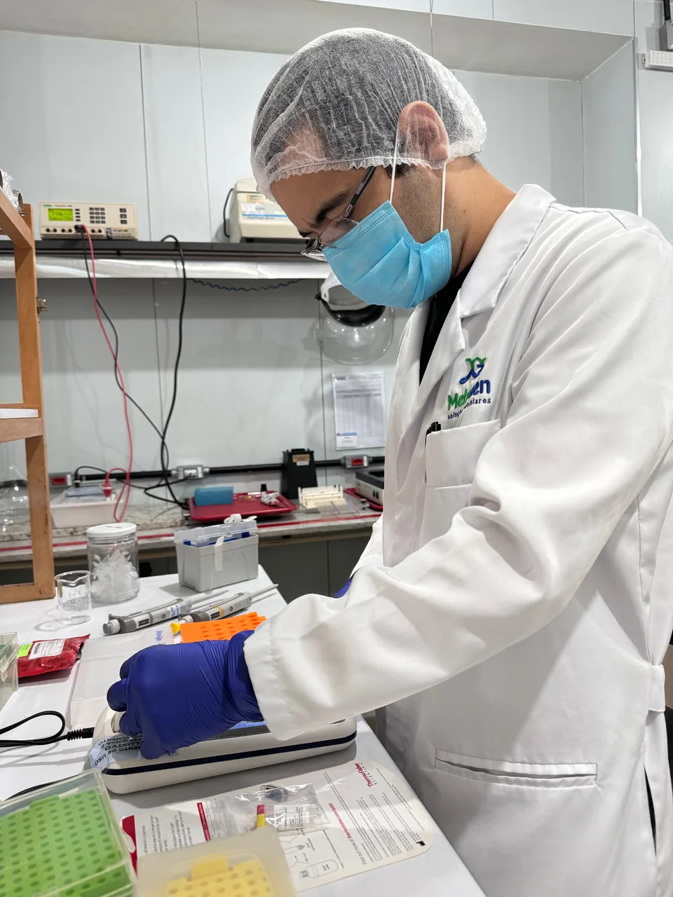Profissional da MetaGen de jaleco e equipamentos de proteção trabalhando em bancada de laboratório.