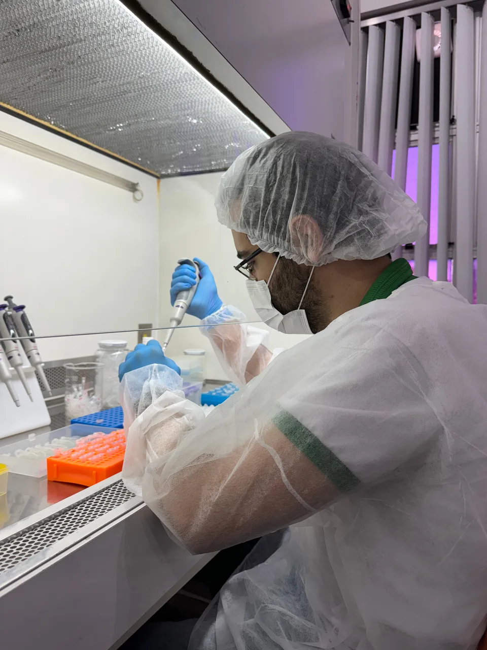Pessoa com equipamentos de proteção realizando pipetagem em laboratório.