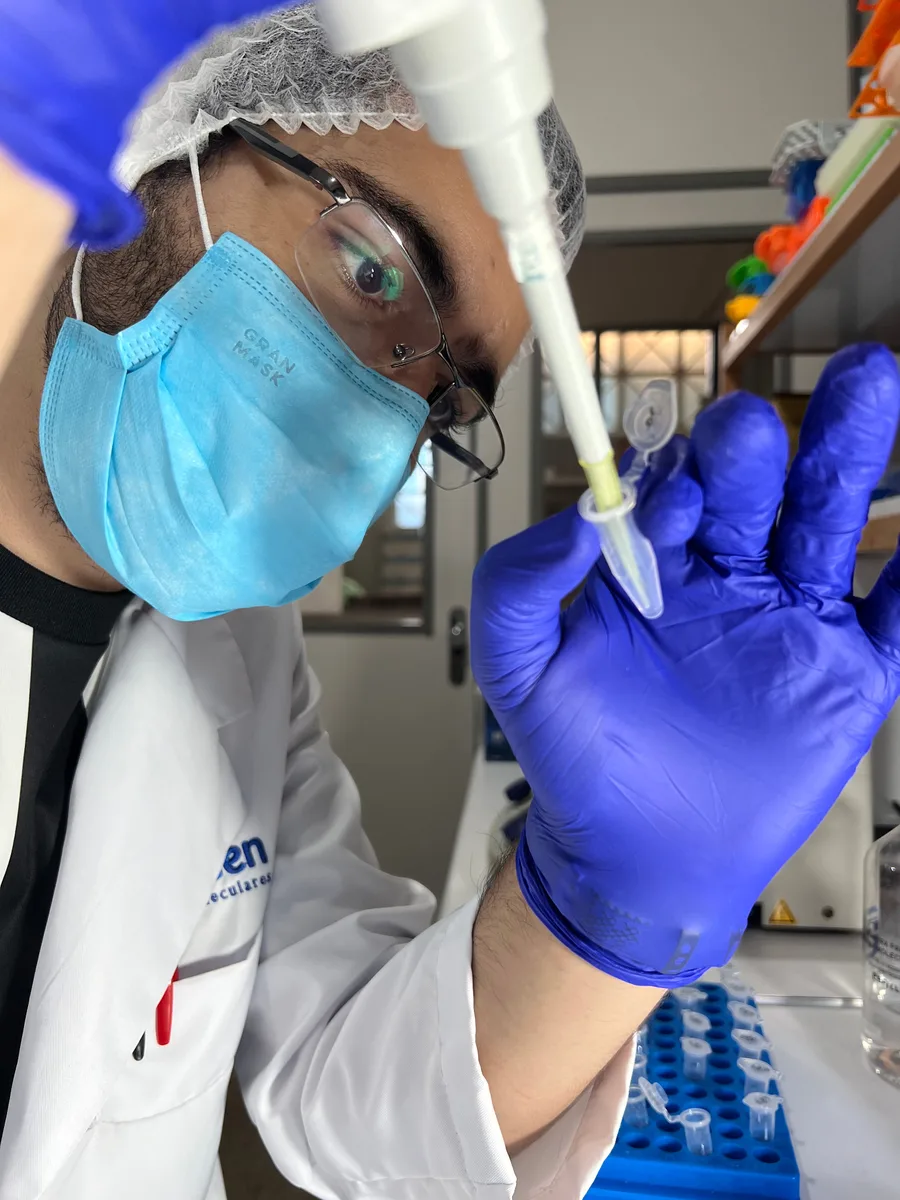 Profissional com equipamentos de proteção manuseando uma pipeta em laboratório.